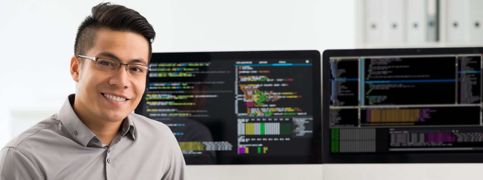 man looking at camera with software coding computer screens behind him