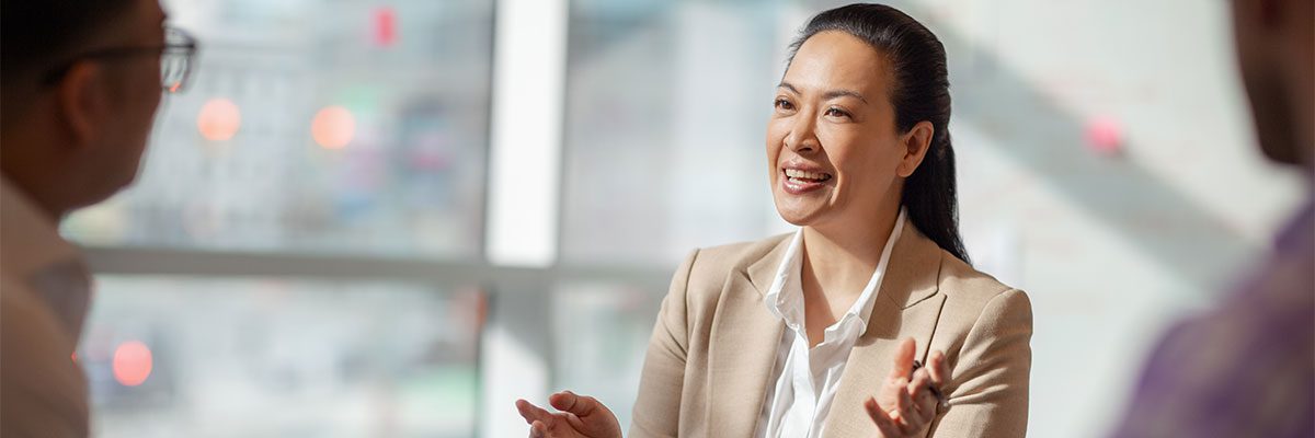 Multiracial Asian Hispanic Pacific Islander mature woman talking with colleagues in business office in meeting