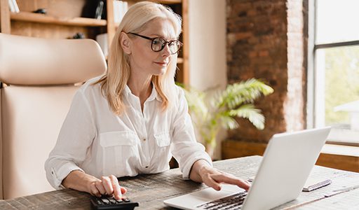 Blonde woman typing on a computer and using a calculator.